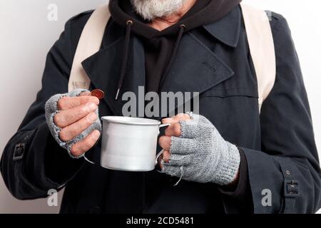 Unkenntlich obdachlos reifen bärtigen Mann in schwarzem Mantel und weißen Rucksack halten Tasse für Geld zu sammeln, in einer Hand eine Münze. Isoliert über weißem Bac Stockfoto