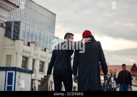 Rückansicht auf reichen Mann beschlossen, armen Mann zu helfen. Junger bärtiger Mann in schwarzem Anzug mit Bettler älterer Mann. Kontrast, verschiedene Segmente der Gesellschaft Stockfoto