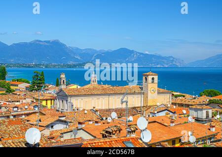 Luftaufnahme von Desenzano del Garda Stadt mit Glockenturm der Duomo di Santa Maria Maddalena Kathedrale Kirche, rot geflieste Dachgebäude, Gardasee Wasseroberfläche, Bergkette, Lombardei, Norditalien Stockfoto