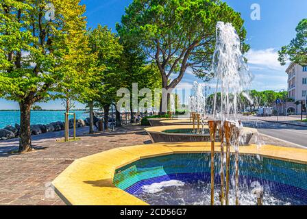 Brunnen und grüne Bäume auf Promenade Böschung des Gardasees im historischen Zentrum von Desenzano del Garda Stadt, Lombardei, Norditalien Stockfoto