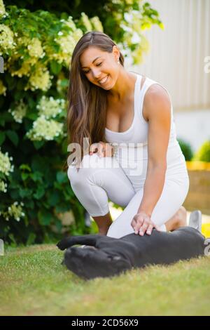 Lächelnd schwangere Frau mit einem großen Bauch streichelt ihr Hund im Garten Stockfoto