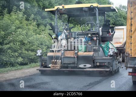 Der Pfleger legt den Asphalt in die Landschaft vor der Kulisse Von grünen Büschen Stockfoto