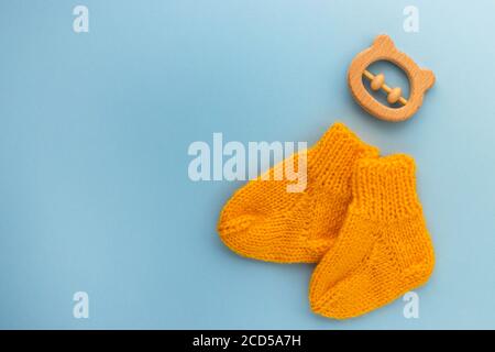 Paar niedliche orange gestrickte Babysocken und hölzerner Beißbär auf blauem Hintergrund. Geburt eines Kindes. Konzept für Neugeborene. Flach liegend, Draufsicht mit Kopierplatz. Stockfoto