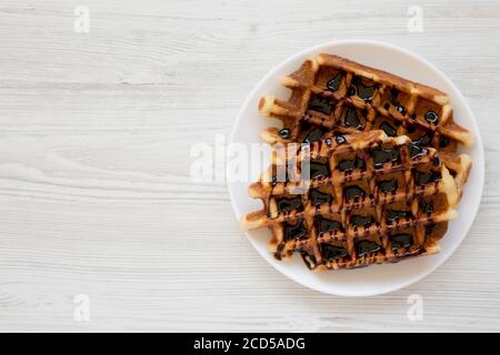 Leckere hausgemachte belgische Zuckerwaffeln auf einem weißen Teller auf einer weißen Holzoberfläche, Draufsicht. Flachlage, über Kopf, von oben. Speicherplatz kopieren. Stockfoto
