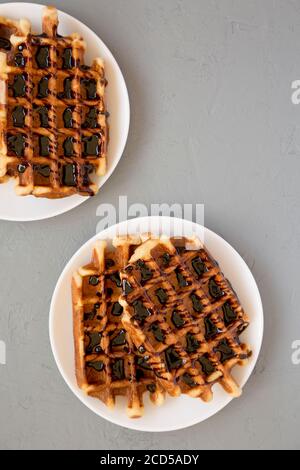 Leckere hausgemachte belgische Zuckerwaffeln auf einem weißen Teller auf einer grauen Oberfläche, Draufsicht. Flachlage, über Kopf, von oben. Speicherplatz kopieren. Stockfoto