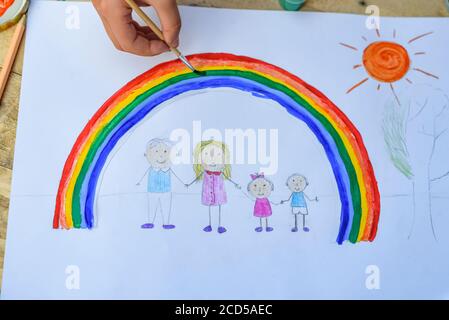 Glückliches Familienkonzept. Kind zeichnet auf ein Blatt Papier: Vater, Mutter, Junge und Mädchen halten die Hände vor dem Hintergrund des Regenbogens und sonnigen Himmels. Nahaufnahme Stockfoto