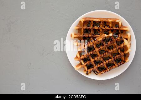 Leckere hausgemachte belgische Zuckerwaffeln auf einem weißen Teller auf einer grauen Oberfläche, Draufsicht. Flachlage, über Kopf, von oben. Speicherplatz kopieren. Stockfoto