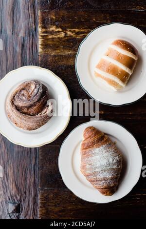 Drei Backwaren (ein Croissant, ein Eisbrötchen und ein Kouign amann) auf einem Holztisch Stockfoto