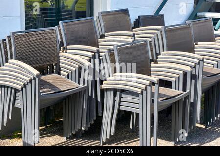 Gestapelte graue Metallstühle mit Armlehnen aus Holz auf der Terrasse eines geschlossenen Restaurants. Stockfoto