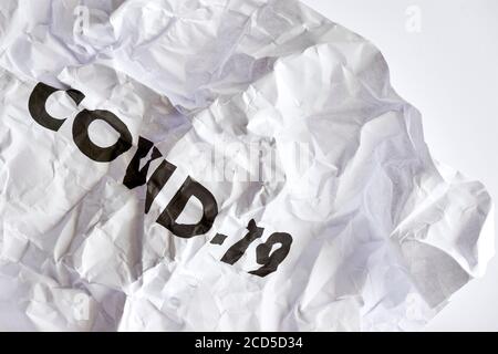 Faltiges weißes Papier mit dem Wort COVID-19 in schwarz gedruckt. Protest gegen Coronavirus Restriktionen Konzept. Stockfoto