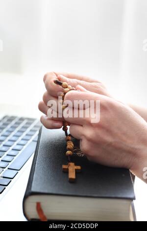 Katholische Messe online. Glauben und Gebet. Eine Frau betet am Rosenkranz. Eine Frau betet auf einem Rosenkranz vor einem Computer. Stockfoto