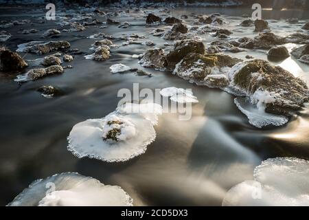 Platten von Eiskristallen auf Felsen im fließenden Fluss Isar In der Nähe von München an kalten nebligen Wintertag Stockfoto