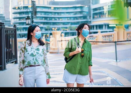Zwei weibliche Freunde asiatische Frau trägt chirurgische Gesichtsmaske im Außenbereich von Dubai Einkaufszentrum. Reisen und Freizeit neue Normalität nach Coronavirus Cov Stockfoto