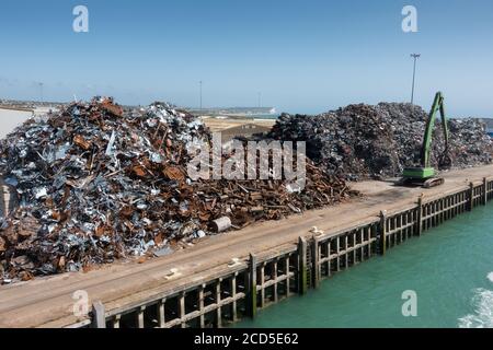 Zwei große Stapel Schrott warten auf den Versand an einem Steg am Dock. In der Entfernung, die für die Sortierung von Materialien verwendet wird, ist ein Bulldozer sichtbar. Stockfoto