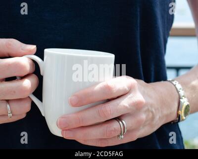 Die Hände der Womans halten einen weißen Becher Tee oder Kaffee Stockfoto