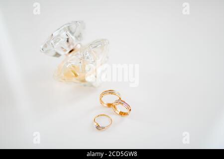 Goldene Eheringe und ein goldener Verlobungsring auf weißem Hintergrund mit einer Flasche Parfüm. Stockfoto