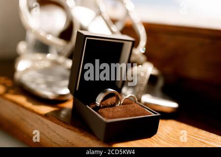 Eheringe in einer offenen braunen Box auf dem Boden mit Damen-Hochzeitssandalen auf einem verschwommenen Hintergrund. Stockfoto