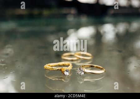 Goldene Eheringe, ein Verlobungsring und ein Folienring auf einem verschwommenen Hintergrund mit Wassertropfen. Stockfoto