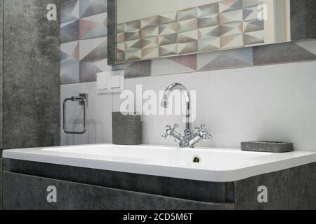 Modernes Badezimmer mit Metallhahn und weißem Keramikwaschbecken. Bad Accessoires und Spiegel. Stockfoto