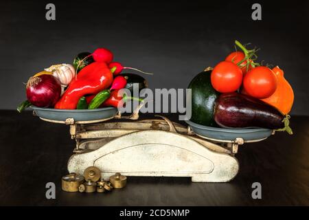 Frisches Gemüse und alte Küchenwaage auf schwarzem Hintergrund. Ernte von Gemüse. Gesunde Ernährung. Stockfoto