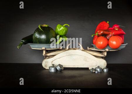 Frisches Gemüse und alte Küchenwaage auf schwarzem Hintergrund. Ernte von Gemüse. Gesunde Ernährung. Stockfoto