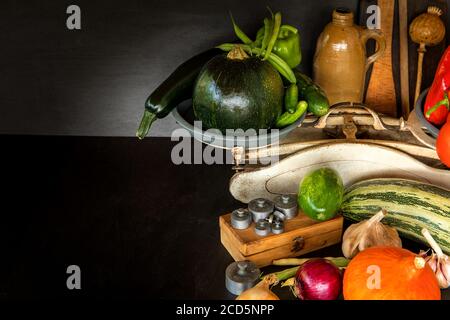 Frisches Gemüse und alte Küchenwaage auf schwarzem Hintergrund. Ernte von Gemüse. Gesunde Ernährung. Stockfoto