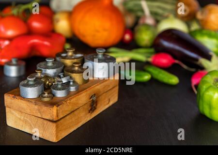 Alte Messinggewichte. Gewichte auf alten Schuppen. Frisches Gemüse und alte Küchenwaage auf schwarzem Hintergrund. Stockfoto
