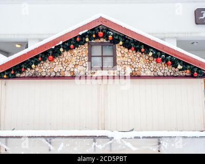 Fragment eines Hauses mit Fenster mit Holzdekor und Weihnachtsschmuck unter dem Dach Stockfoto