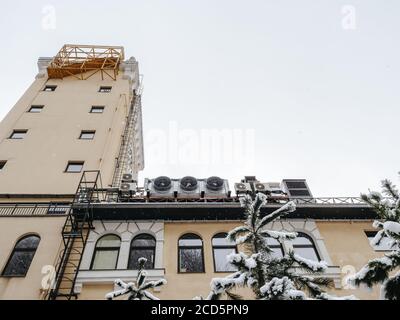 Die Spitze des Gebäudes mit einem Turm, Fenstern und Feuerleitern mit schneebedeckten Tannen im Vordergrund. Ansicht von unten nach oben Stockfoto