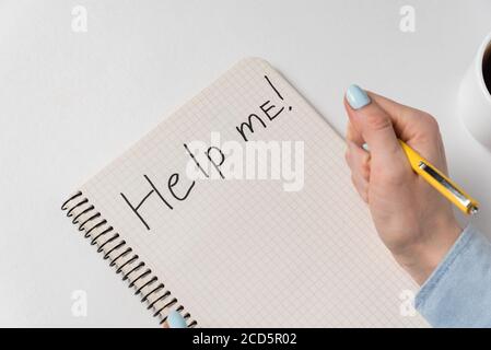 Hilf mir auf Notizbuch über weißem Hintergrund geschrieben. Weibliche Hand schreiben im Copybook. Stockfoto