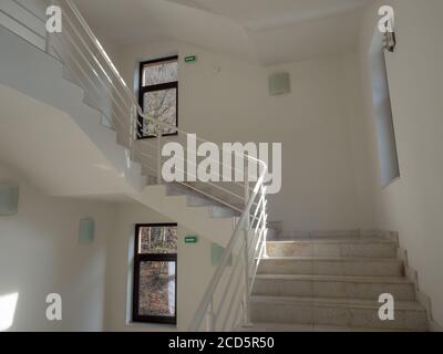 Eine Treppe mit hellen Stufen mit weißem Geländer und weiß Wände und Fenster in dunklen Rahmen Stockfoto