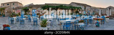 Tische und Stühle in traditionellen italienischen Restaurants auf dem Hauptplatz des historischen Dorfes Marzamemi, Syrakus, Sizilien an einem sonnigen Tag eingerichtet. Stockfoto