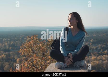 Schöne junge Frau sitzt auf einem Hügel und blickt in die Ferne. Reisen Sie für das Wochenende. Stockfoto