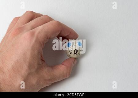 Männliche Hand hält gesägtes Ei mit großen Augen. Ei mit lustigen Gesicht auf weißem Hintergrund. Stockfoto