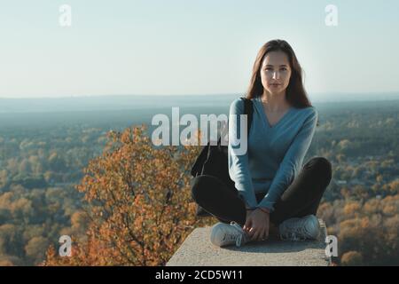 Junge Frau sitzt auf einem Hügel auf dem Hintergrund der Natur. Blickpunkt. Hochformat Stockfoto