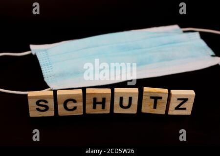 Gesichtsmaske mit dem Wort SCHUTZ in Deutsch buchstabiert Mit Holzblöcken auf schwarzem Hintergrund Stockfoto