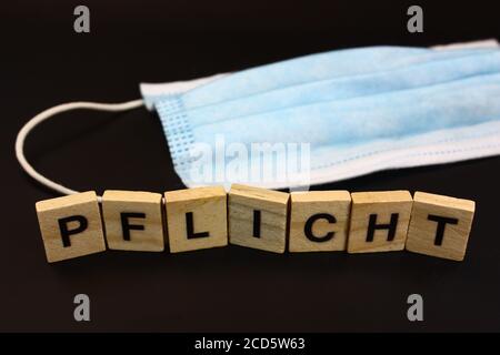 Gesichtsmaske mit dem Wort OBLIGATORISCH in Deutsch buchstabiert Mit Holzblöcken auf schwarzem Hintergrund Stockfoto