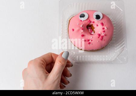 Weibliche Hand und lustige Donut mit großen Augen in Kunststoffbehältern. Ökologie Konzept. Stockfoto