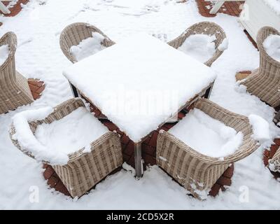 Korbsessel mit Schnee stehen um einen schneebedeckten Tisch herum Auf einer schneebedeckten Fläche Stockfoto