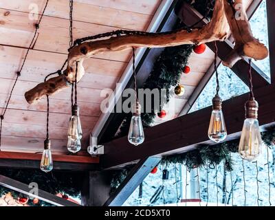 Unter dem Dach eines Holzhauses hängen an einem gebogenen Holzbalken Glühbirnen. Weichzeichnungseffekt Stockfoto
