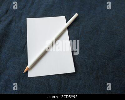 Ein weißes Blatt Papier mit einem weißen Graphitstift Liegt auf einer blauen Stoffoberfläche Stockfoto