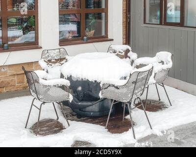 Ein Tisch mit dunkler Bettwäsche und Stühlen drum herum Stellen Sie sich unter die mit Schnee übersäten Fenster Stockfoto