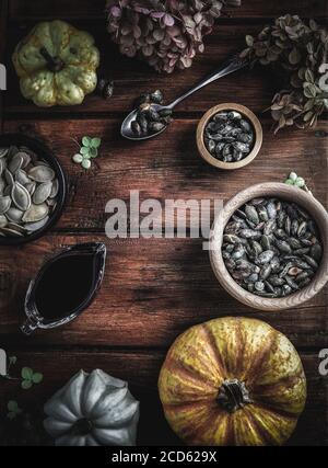 Trockene Hortensien, Kürbisse, Kürbisöl und Samen in Holzschüsseln auf Vintage-Holztisch. Herbstkonzept. Overhead-Aufnahme. Stockfoto