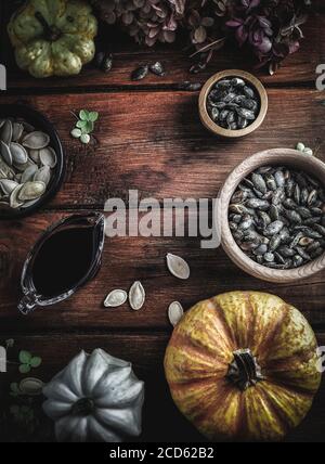 Trockene Hortensien, Kürbisse, Kürbisöl und Samen in Holzschüsseln auf Vintage-Holztisch. Herbstkonzept. Overhead-Aufnahme mit Kopierplatz. Stockfoto