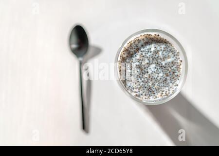 Chia Samen Pudding in Mandelmilch - gesund vegan essen Frühstück am Morgen. Draufsicht auf Küchentisch mit schwarzem Löffel und Glasbecher Stockfoto
