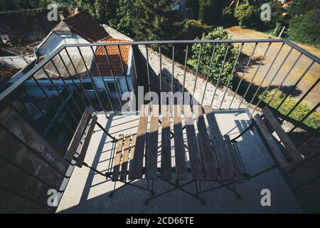 Weitwinkelansicht eines kleinen gemütlichen Balkons eines Wohnhauses oder eines Landhauses mit einem Sommergittertisch und zwei Stühlen, die Morgensonne Stockfoto