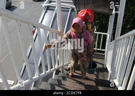 Bekasi, Indonesien. August 2020. Eine Frau, die Jamu (traditionelles Kräutergetränk) in einer Maske verkauft, trägt ihre Waren mit einem Bambuskorb hinter ihrem Rücken auf einer Fußgängerbrücke in der Innenstadt von Bekasi. Inmitten des Ausbruchs der Corona-Virus-Pandemie ist das Trinken traditioneller Kräuter eine Möglichkeit für Menschen, ihre Immunität zu erhöhen, damit sie nicht leicht krank werden. (Foto von Kuncoro Widyo Rumpoko/Pacific Press) Quelle: Pacific Press Media Production Corp./Alamy Live News Stockfoto