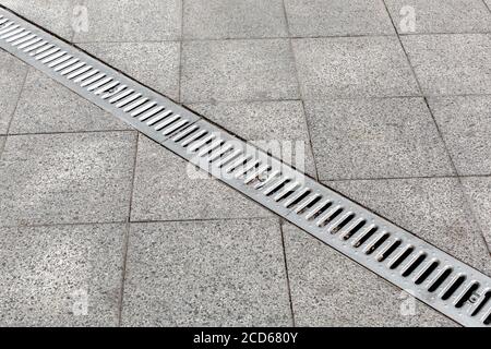 Grabenabfluss grau mit Stahlreinigungsrost auf Granitstein Fliese Straßenverbesserung der Stadt, Nahaufnahme Details Entwässerungssystem, niemand. Stockfoto