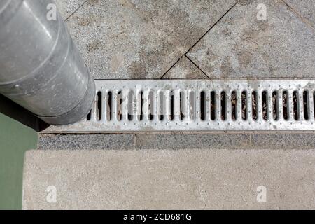 Städtebauliche Struktur Abflussrohr mit einem Entwässerungsrost für die Entwässerung Von Regenwasser vor dem Hintergrund eines Gehwegs aus Granit aus Stein Vom Quadrat til Stockfoto