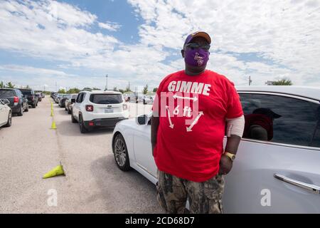 Austin, TX USA 26. August 2020: Hunderte von Autos aus der Küste von Ost-Texas und dem Südwesten Louisianas warten in der Schlange an einem Hurricane Laura Evakuierungszentrum auf dem Circuit of the Americas Rennbahn Parkplatz. Nachdem er Stunden in seinem Auto verbracht hat, bekommt Ronnie Ruffin von Lake Charles, LA, frische Luft, während er eine Maske und ein 'Gimme 6 Feet' T-Shirt trägt. Laura wird voraussichtlich über Nacht als Sturm der Kategorie 4 landen und verheerende Schäden an der Küste von Texas und Louisiana und im Landesinneren anrichten. Kredit: Bob Daemmrich/Alamy Live Nachrichten Stockfoto